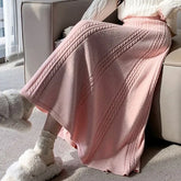 Pink knitted blanket draped over a person sitting on a couch.